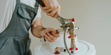 A plumber tightening a water heater connection with two wrenches.