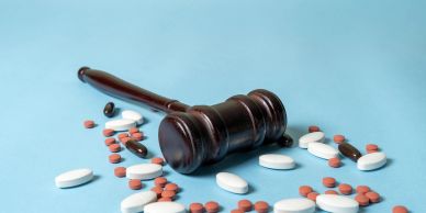 A gavel and scattered pills on a blue surface.
