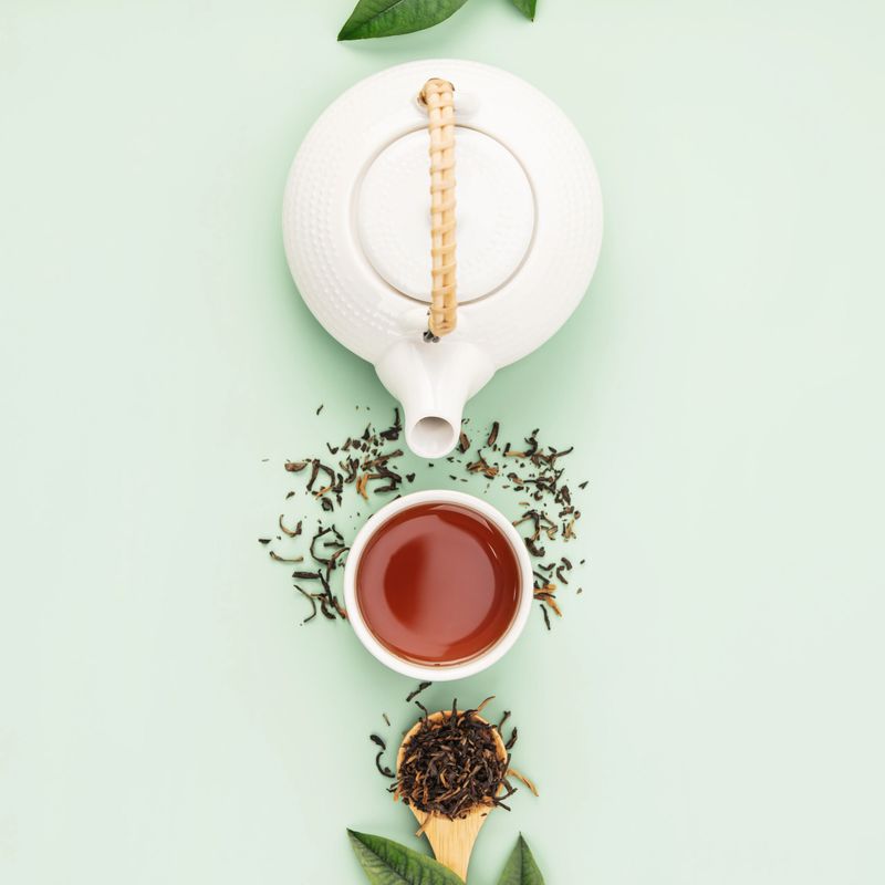 A pristine white teapot with a bamboo handle and a cup of tea surrounded by loose leaves on a soft pastel background create a serene tea time scene...