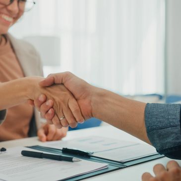 Two people shaking hands over a signed contract with a pen on the table.