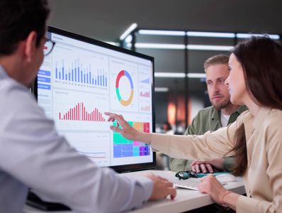 Three colleagues analyzing graphs and charts on a large computer screen.