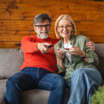 Elderly couple enjoying TV time and dessert on the couch.