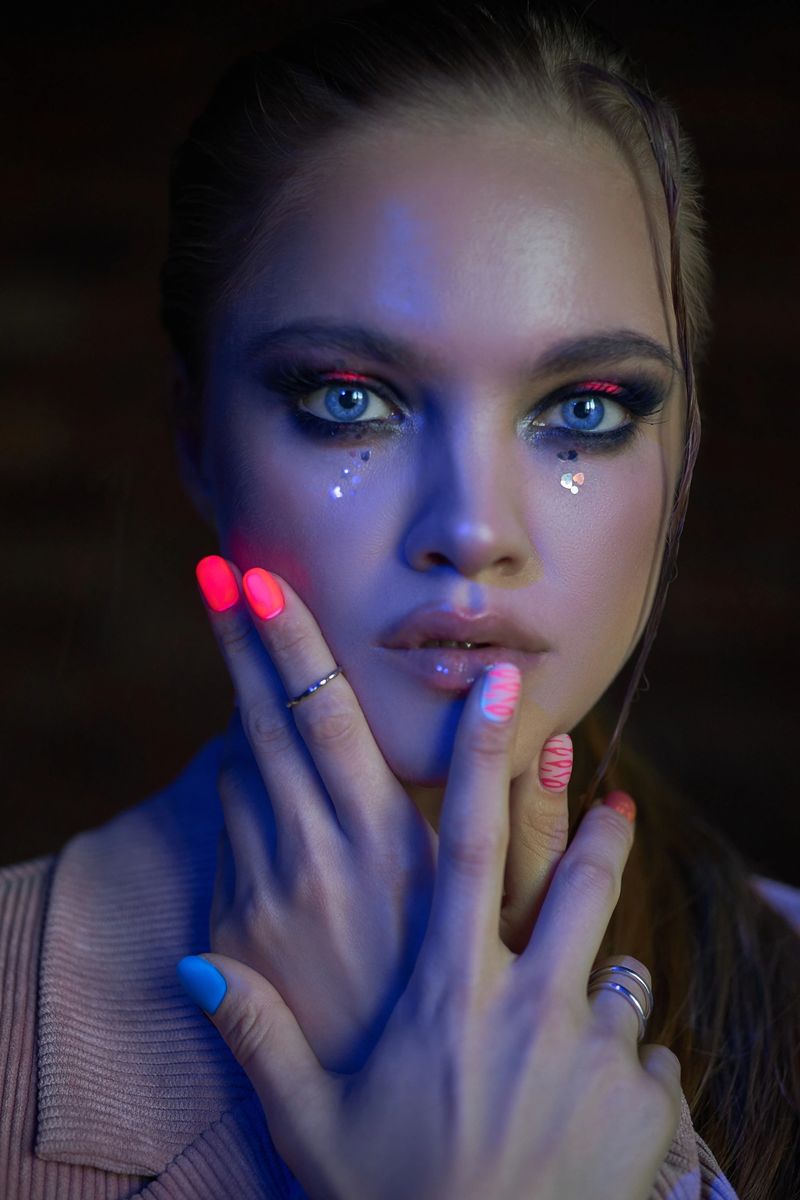 model showcases a captivating expression with bold eye makeup and colorful nails while striking a pose in a creatively lit studio, highlighting her unique beauty.