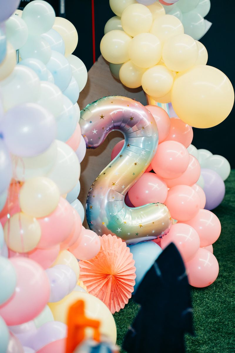 Vibrant balloon decor featuring a large shiny rainbow number two surrounded by pastel balloons, creating a festive atmosphere for a child's second birthday celebration