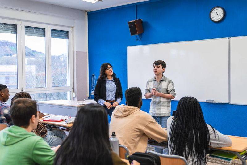 High school student delivering an engaging presentation in front of classmates and a teacher, showcasing skills in public speaking and communication