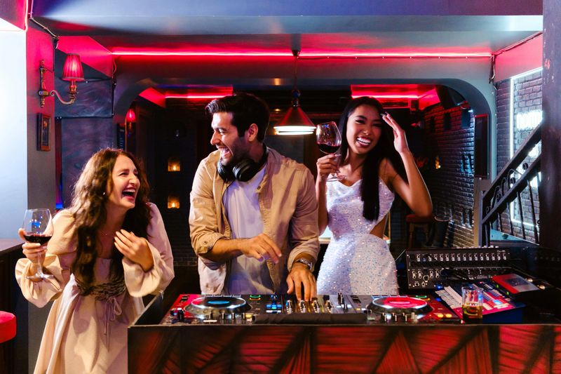 Diverse group of friends enjoying girl's night out at a nightclub, laughing and dancing near DJ booth with wine glasses, vibrant neon lights, and upbeat atmosphereperfect for nightlife, celebration