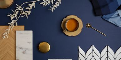Elegant flat lay of blue-themed decor with coffee, gold accents, and white leaf tiles.