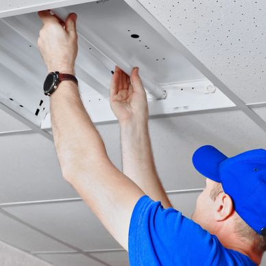Man in blue shirt and cap replacing a ceiling light tube.