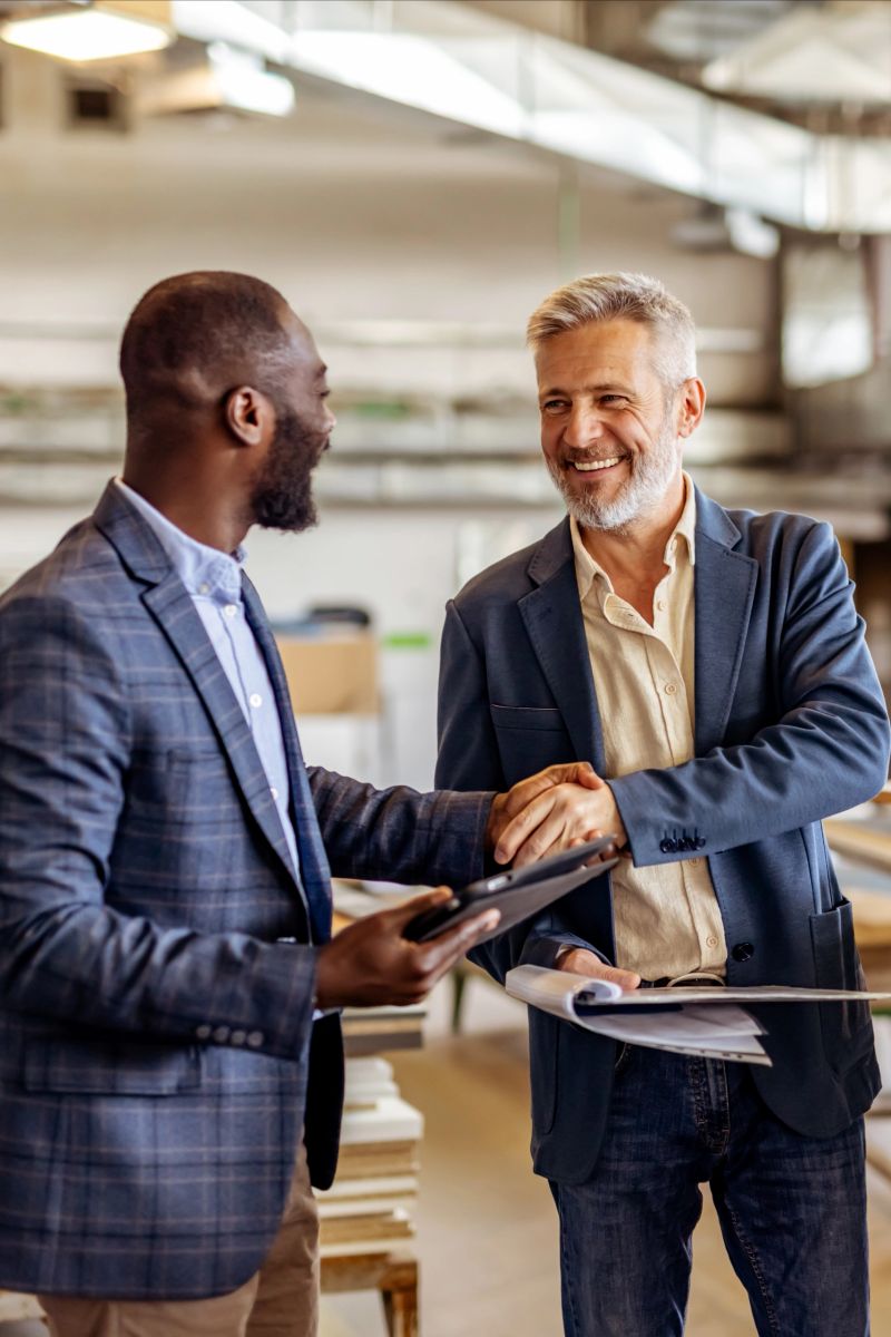Two professionals in jackets sharing a handshake in a modern office, symbolizing business collaboration, partnership, and professional success. Their engagement conveys a sense of teamwork, making agreements, and friendly connection.