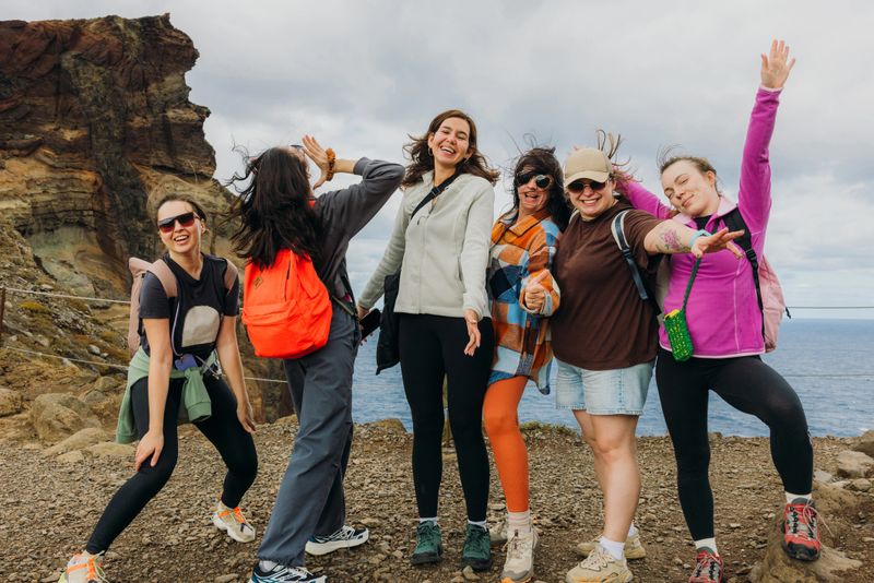 Large group of five female friends wearing sport clothes having fun and feeling happiness while hiking at the scenic footpath with cliffs and ocean view at Porto Do Sao Lourenco on Madeira island, Portugal
