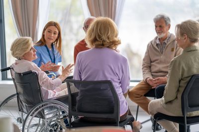 A group of seniors and a caregiver in a supportive discussion circle.