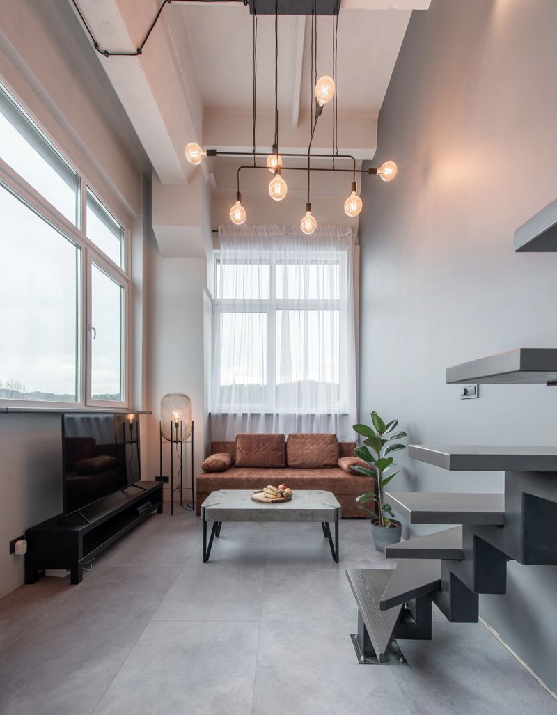 Bright and elegant loft living room featuring a minimalist decor, natural light-filled ambiance, and a cozy sofa contrasted by industrial-style details and modern aesthetics