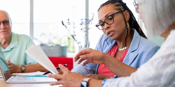 A woman explains documents to two older adults during a meeting.