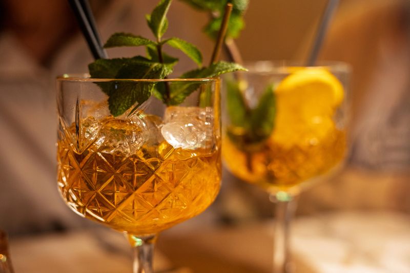 Two beautifully crafted cocktails sit on a wooden table, garnished with sprigs of mint and slices of lemon. The warm atmosphere suggests a delightful evening with friends.