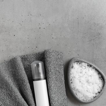 White spray bottle and bowl of coarse salt on a gray surface with a textured cloth.
