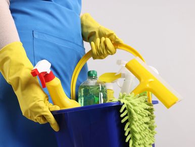 Person holding a blue bucket filled with cleaning supplies wearing yellow gloves.