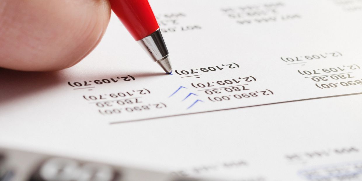 Person marking calculations on a financial document with a red pen.
