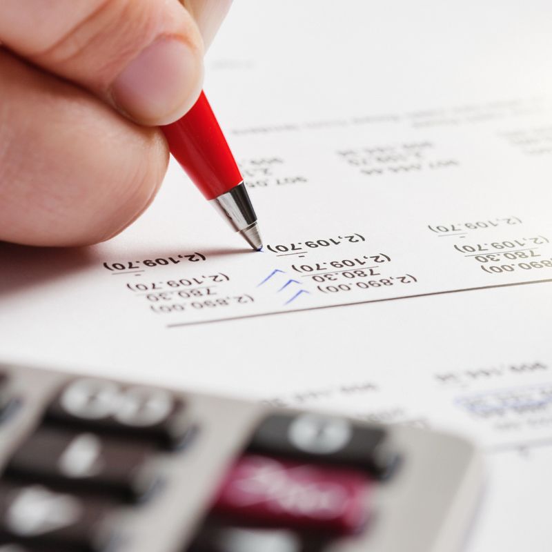 Extreme close-up of a person's hand checking financial figures on a printout of a spreadsheet.