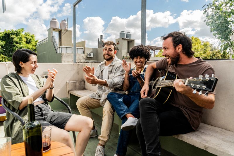 Friends having fun playing acoustic guitar and clapping on rooftop