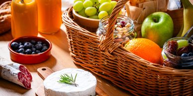 A picnic basket with fruits, cheese, and juice on a wooden table.