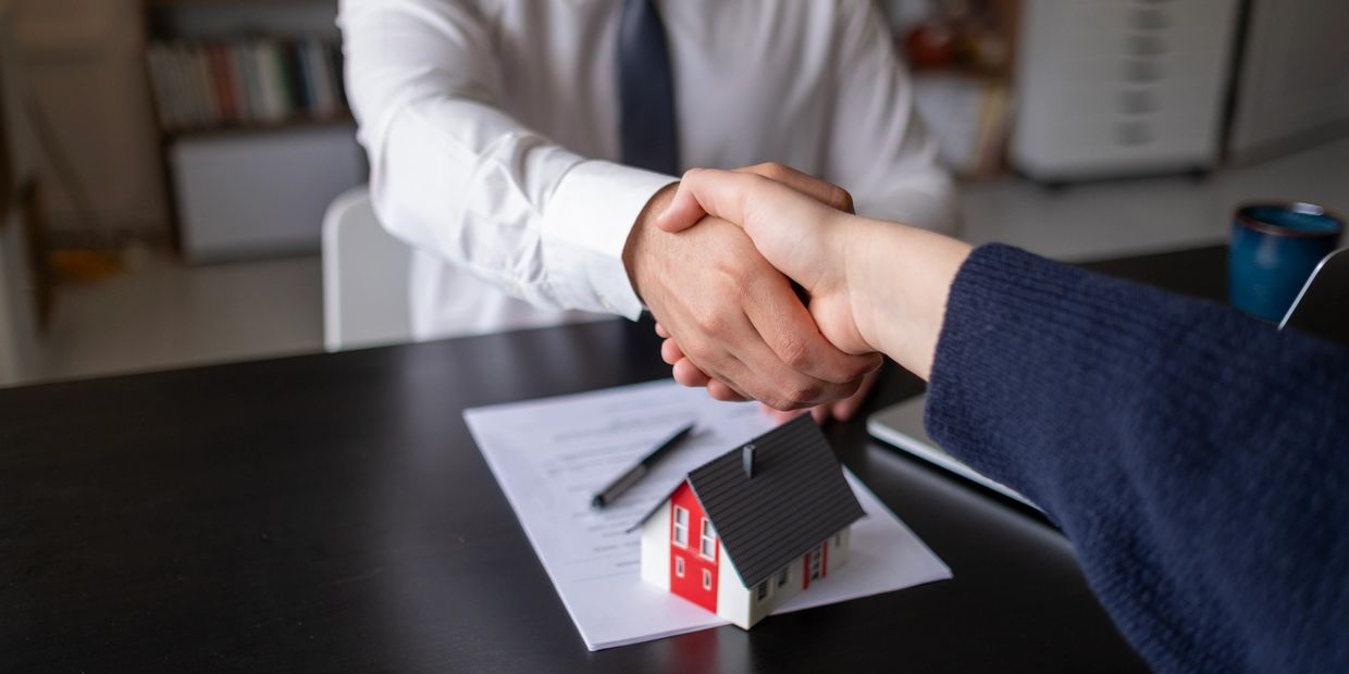 Two people shaking hands over a house contract model on a table.