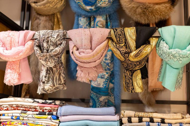 A collection of vibrant scarves hangs neatly in a boutique. Each scarf displays unique patterns and textures, showcasing an array of colors and styles perfect for various outfits.
