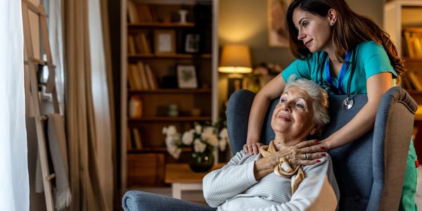 Nurse comforting an elderly woman in a chair.