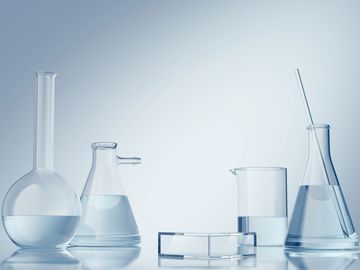 Various transparent chemistry glassware filled with clear liquid on a white surface.