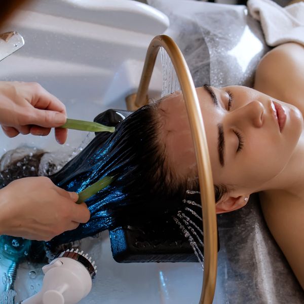 Woman enjoying a relaxing hair wash with aloe vera treatment at a salon.