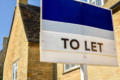 A 'To Let' sign outside a traditional stone house on a sunny day.
