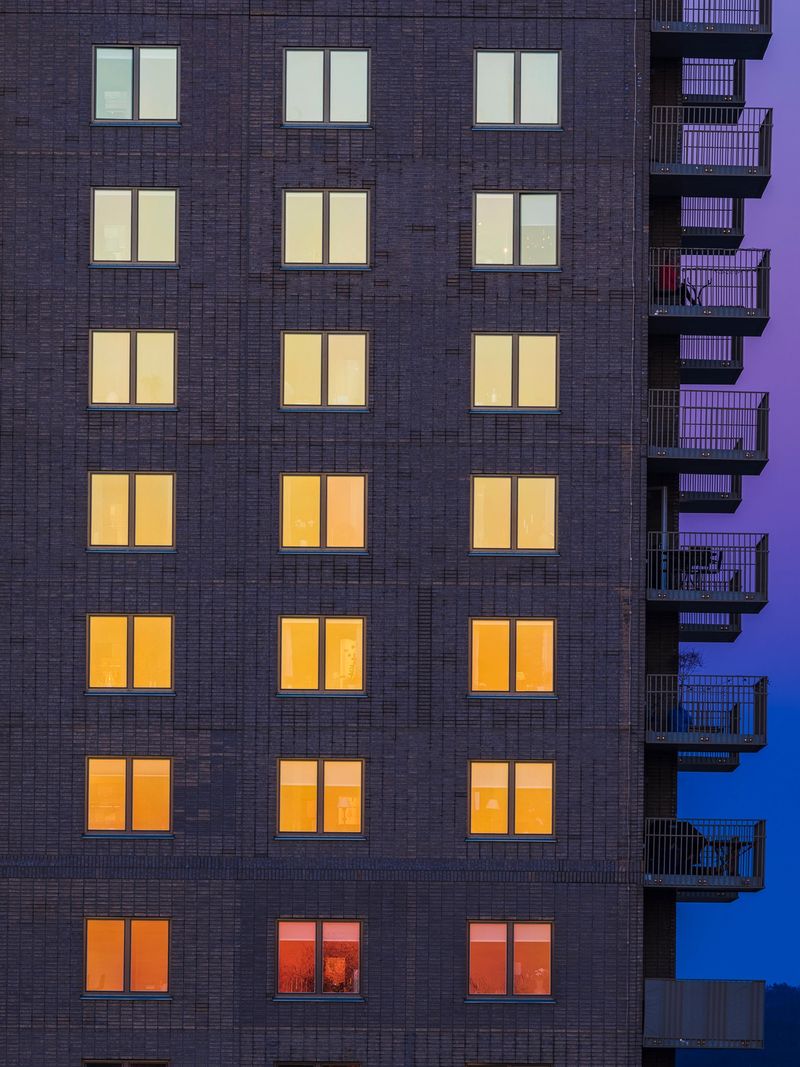 Warm hues from the setting sun illuminate the windows of a modern residential building in Gothenburg, creating a striking visual effect amidst the twilight sky.
