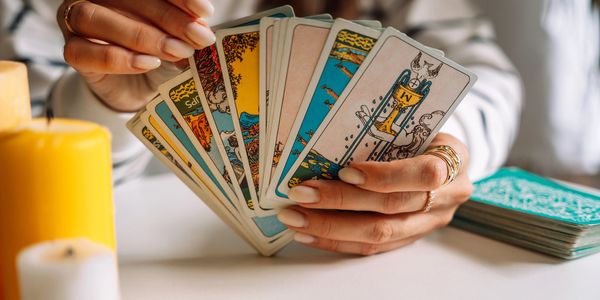 Person holding a fan of tarot cards with candles nearby.