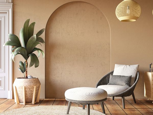 Cozy reading nook with wicker chair, ottoman, and potted plant in a neutral-toned room.