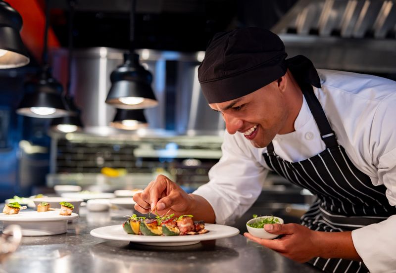 Happy Latin American chef decorating a plate while serving food at a restaurant and smiling