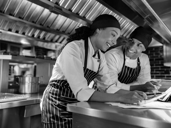 Two chefs in a commercial kitchen reviewing recipes and smiling.