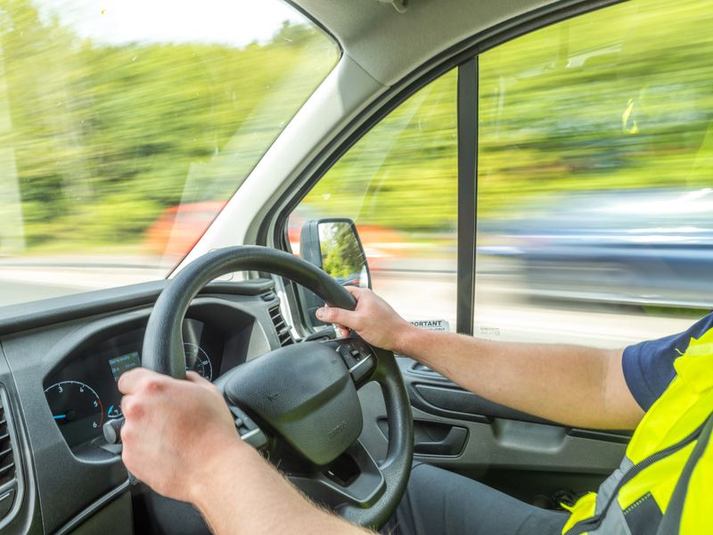 A delivery driver in a high-visibility vest navigates a busy motorway in the UK during daytime. Perfect for logistics, transportation, or road safety campaigns.