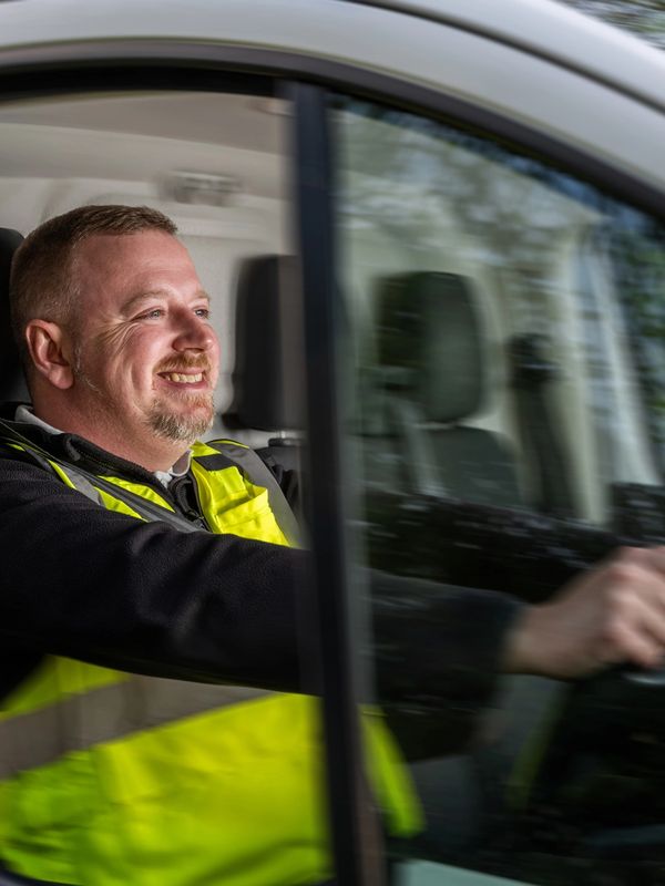 Smiling man in a yellow safety vest driving a vehicle.