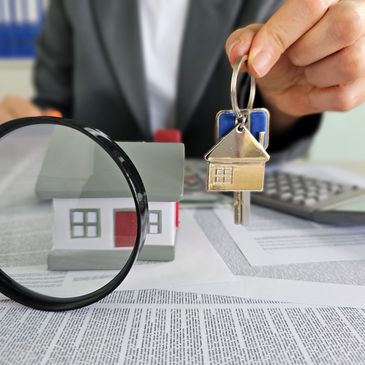 Person holding house-shaped keychain near a model house and documents.