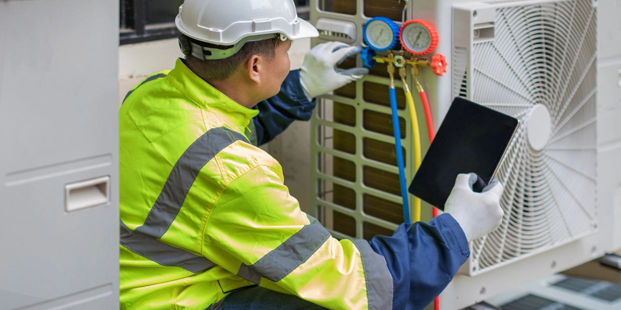Technician inspects HVAC unit using gauges and tablet.