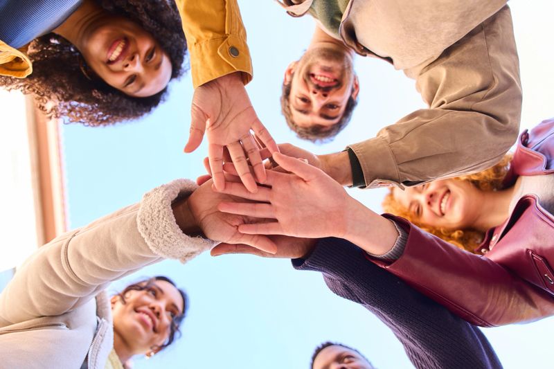 Students joining hands in a display of teamwork and unity, celebrating collaboration and support under a bright, clear sky