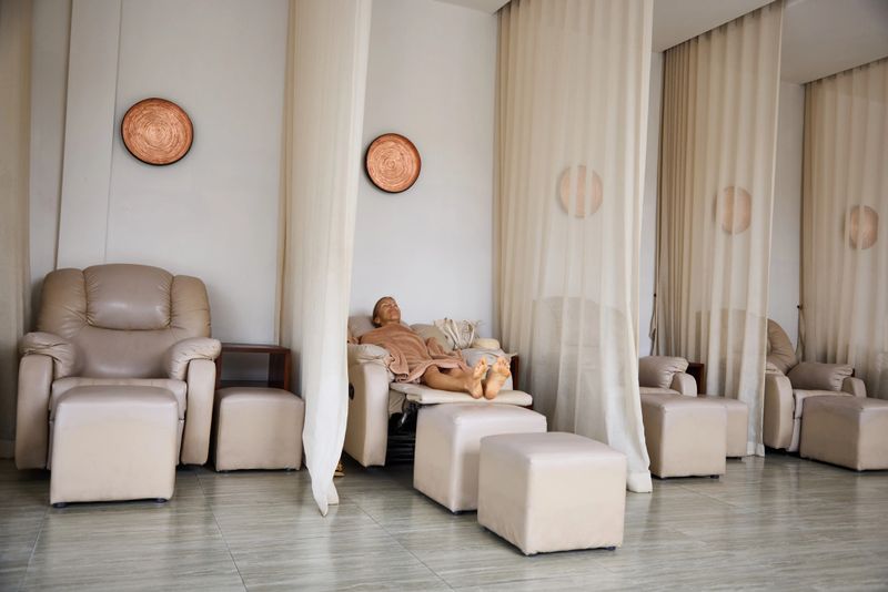 A Black woman in a tranquil spa recliner, draped in soft linen, resting peacefully in a warmly lit healing sanctuary.