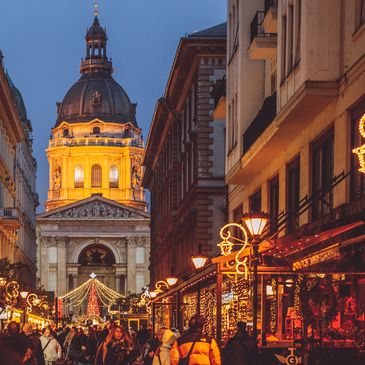 Festive street with Christmas lights and a grand illuminated building at dusk.
