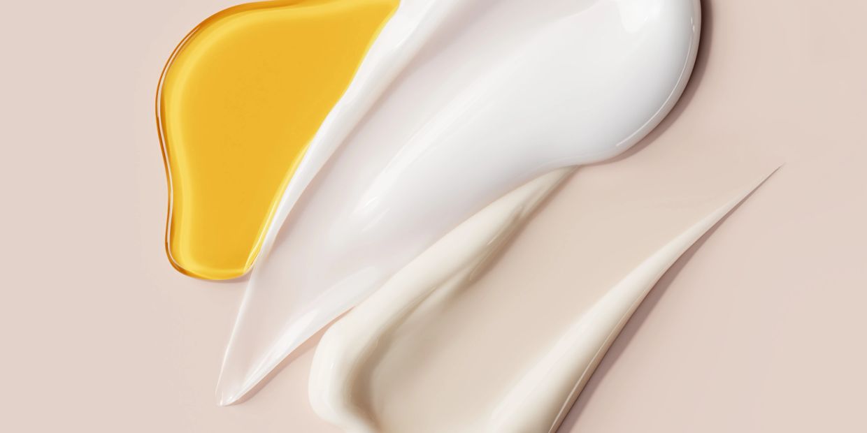 Various beauty product textures in yellow, white, and beige tones on a pastel background.