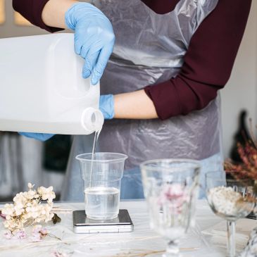Person pouring liquid into a plastic cup while wearing gloves and apron.