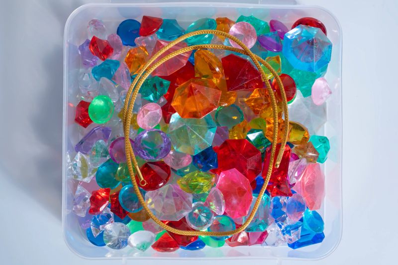 Gold chain with colorful gemstones inside a clear plastic box against a white background, perfect for jewelry and luxury-themed visuals