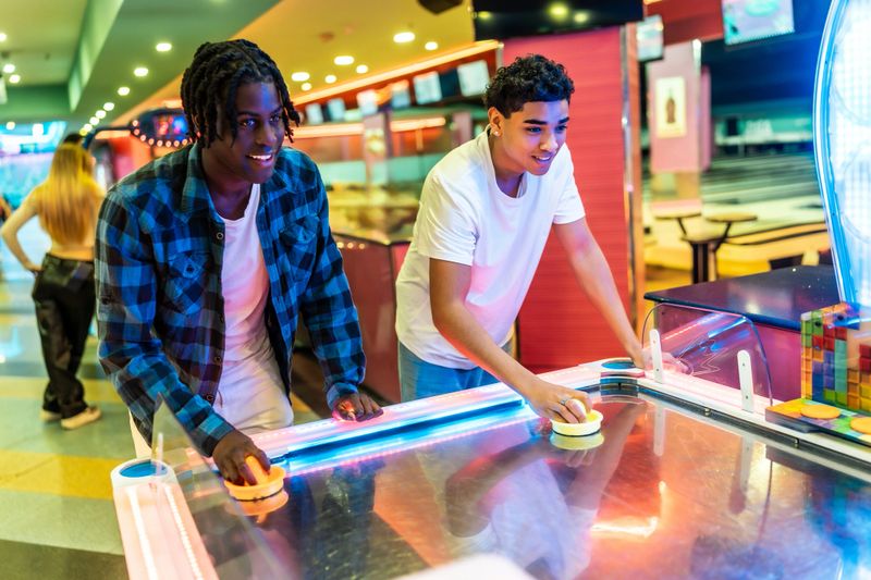 Two multi-ethnic teenage boys enjoying a friendly game of air hockey in a vibrant amusement arcade