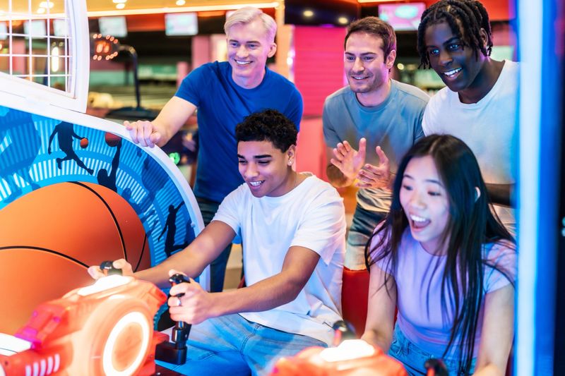 Multiethnic friends enjoying a lively moment while playing arcade basketball at a vibrant bowling alley, sharing laughter and excitement