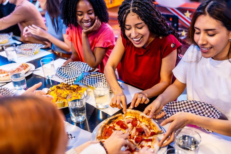 Multiethnic female friends enjoying pizza and nachos together at a bowling alley restaurant, celebrating friendship and good times