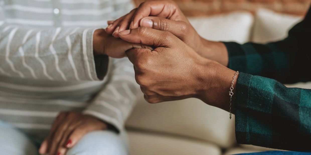 A brown skinned woman holding the hands of another brown skinned woman, in a tender embrace of care.