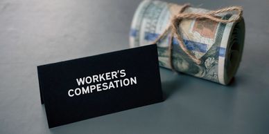 Rolled dollar bills tied with string next to a 'Worker's Compensation' sign.